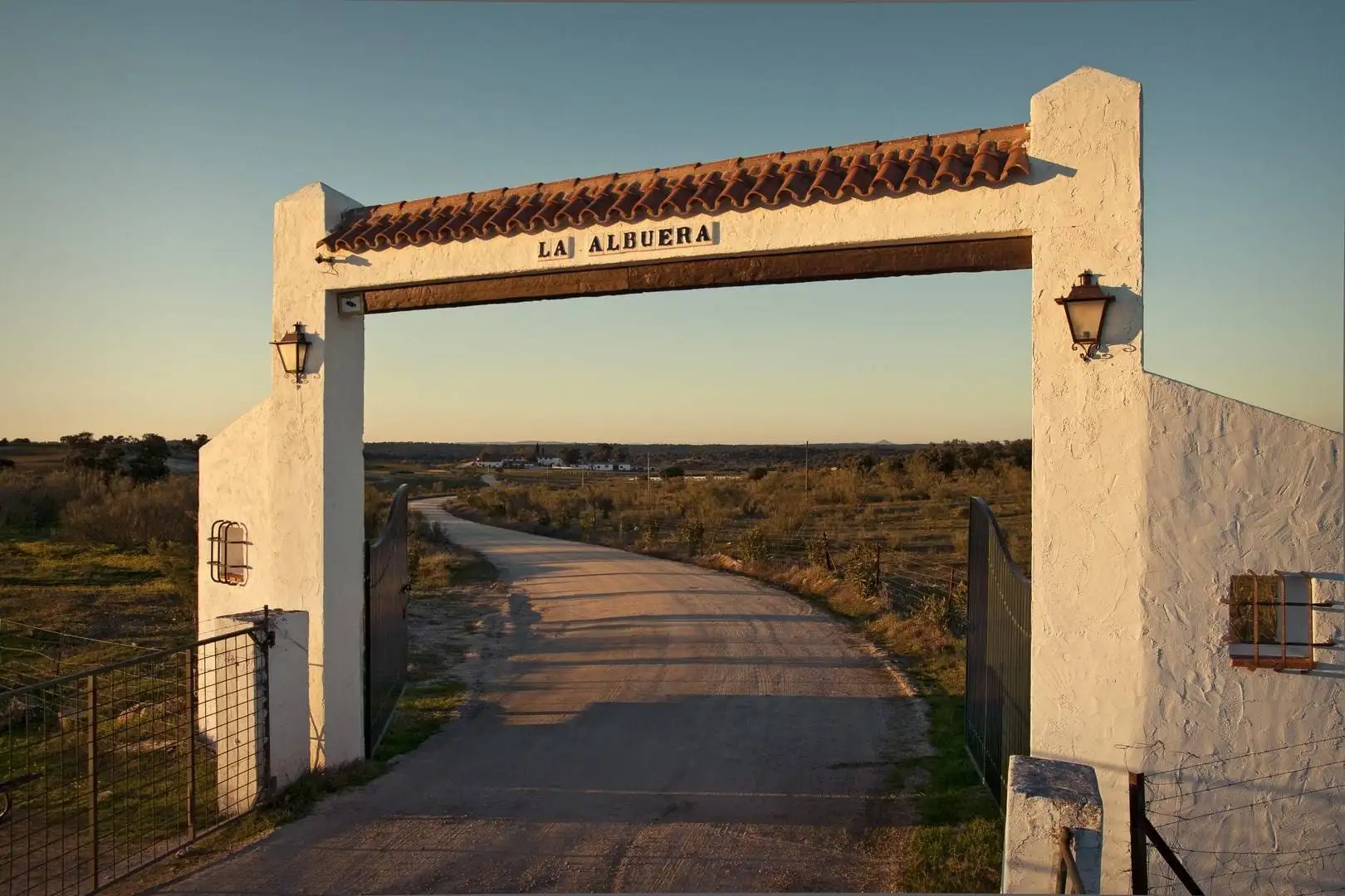 El arco blanco de la entrada, con el nombre de la finca, y el camino al atardecer