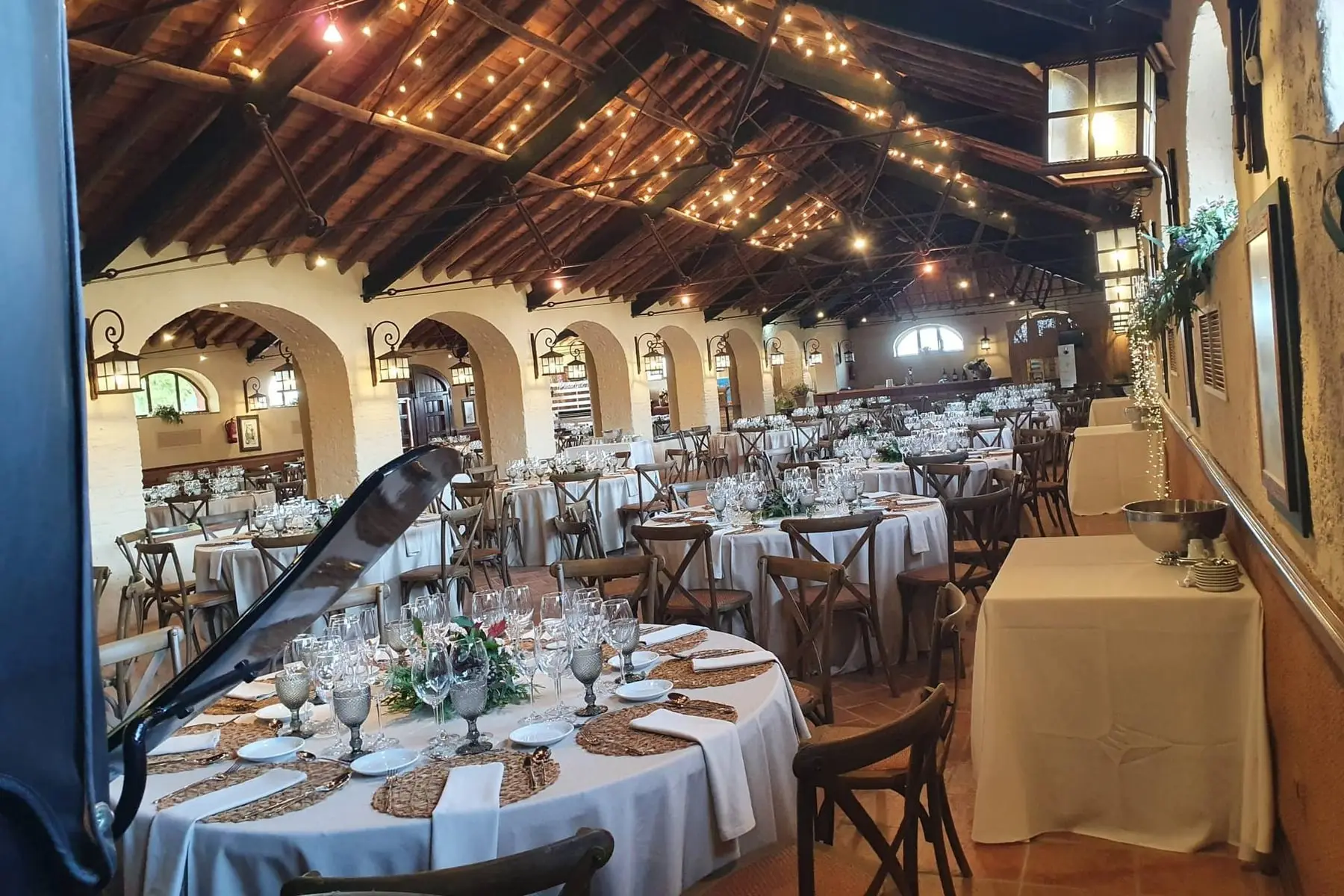 El gran salón de vigas de madera, con mesas redondas y guirnaldas de luces